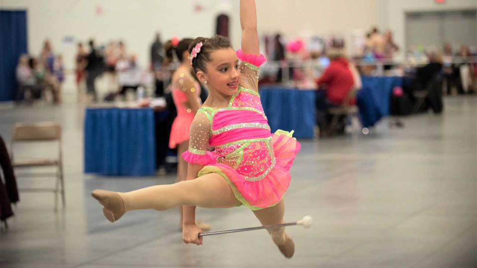 Young girl in a pink leotard twirling a baton.